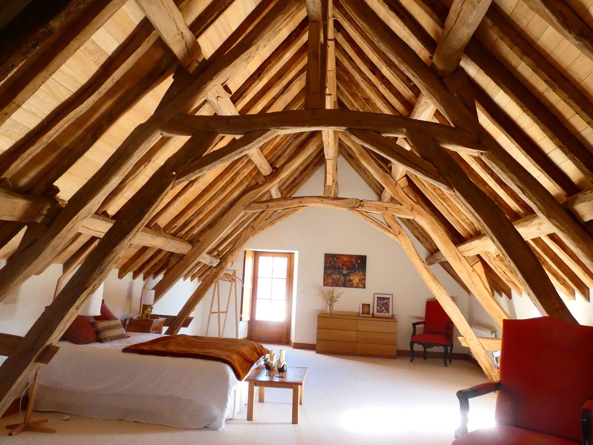 A bedroom with a sloped ceiling, wooden beams, a bed, a dresser, and a chair.