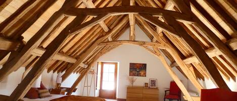 A bedroom with a sloped ceiling, wooden beams, a bed, a dresser, and a chair.