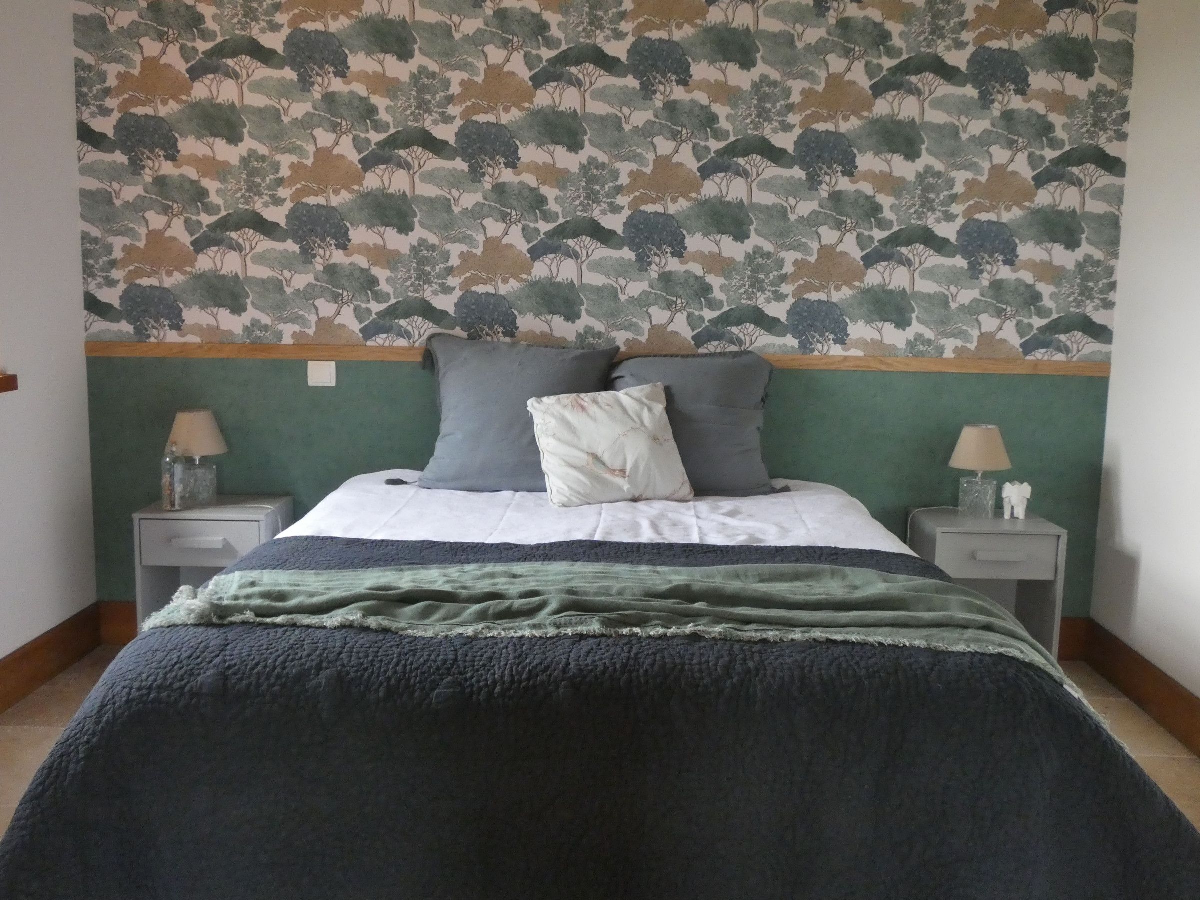 Un dormitorio con cama, dos mesitas de noche, papel tapiz estampado y cabecera verde.