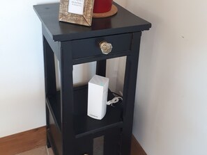 A black nightstand with a drawer and a shelf, holding a white electronic device and a small framed item.