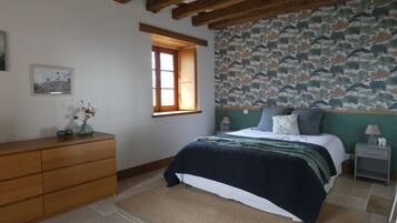 A bedroom with a bed, wooden dresser, a window, and a patterned wallpaper.