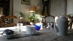 A dining table with a teapot, cups, and saucers, surrounded by chairs and potted plants. - Comfortable rooms on a farm in the heart of Berry (Montchevrier)