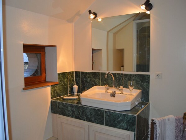A bathroom with a white sink, green marble tiles, a mirror, and a wooden medicine cabinet.