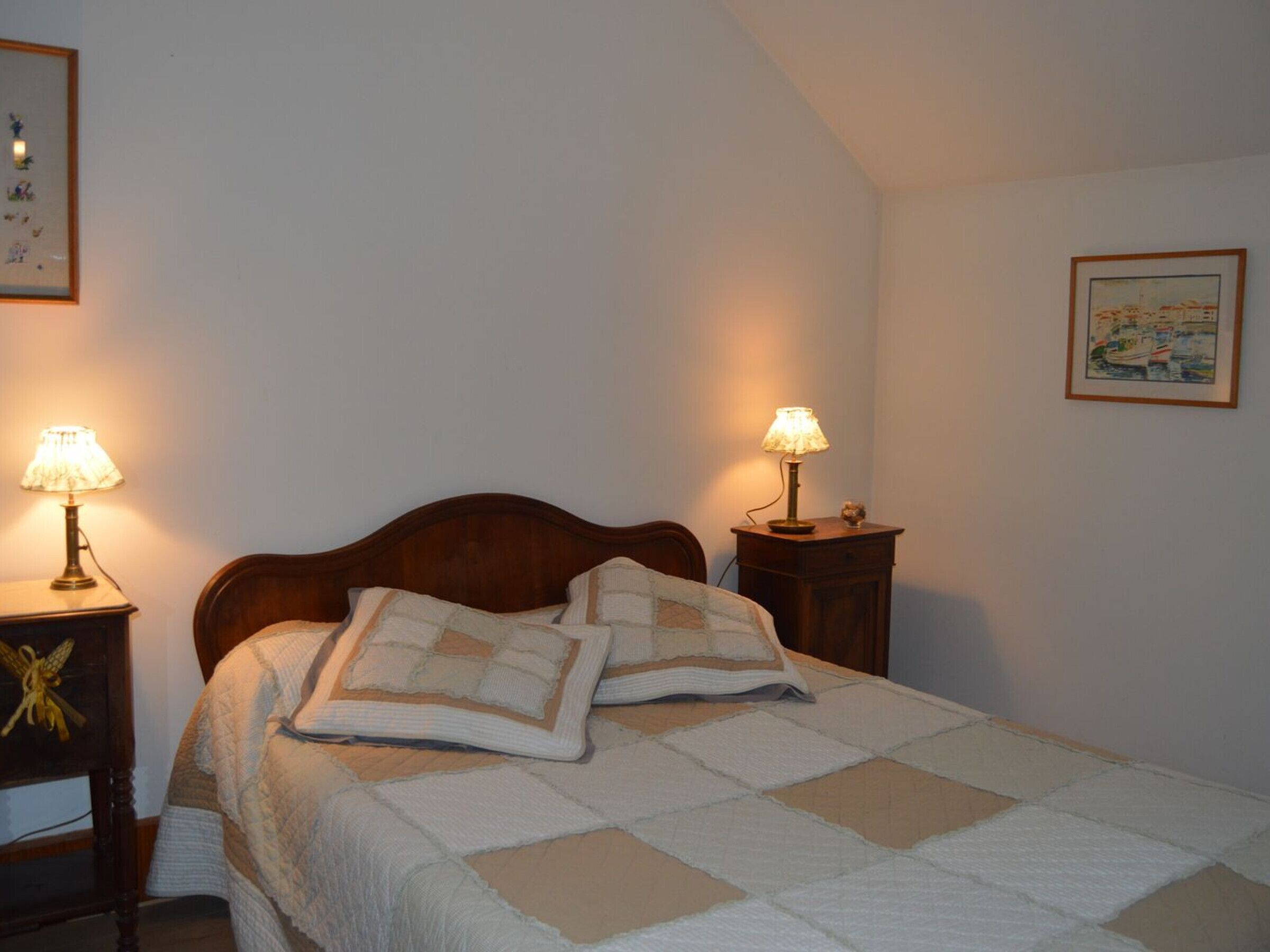 A bedroom with a wooden bed, two bedside lamps, a quilted bedspread, and a framed map on the wall.