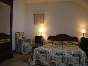 A bedroom with a bed, two chairs, a nightstand, a lamp, and a framed picture on the wall.
