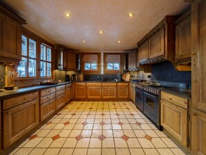A spacious kitchen with wooden cabinets, a tiled floor, and a large stove.