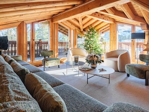 A cozy living room with a wooden ceiling, large windows, a sofa, a coffee table, and a potted plant.