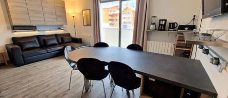 A modern kitchen with a dining table, chairs, a sofa, and a TV.
