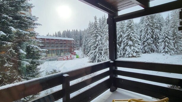 Een houten balkon met uitzicht op met sneeuw bedekte bomen en een gebouw op de achtergrond.