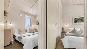 A bedroom with two beds, wooden walls, a window, and a framed picture on the wall.