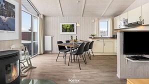 A modern kitchen with a dining area, featuring a large flat-screen TV, a wood-burning stove, and a dining table with chairs.