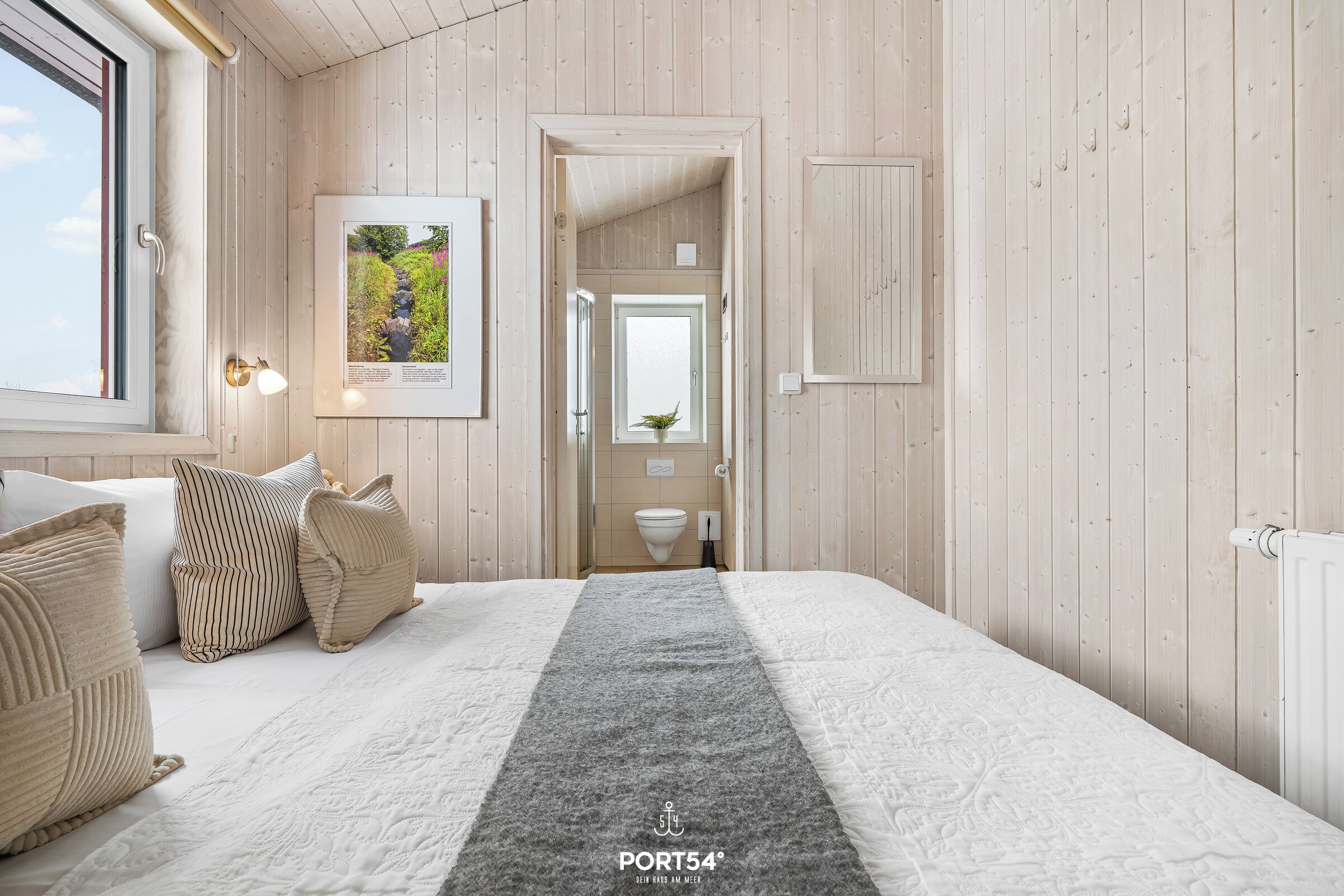 Ein Hotelzimmer mit Holzvertäfelung, einem Bett mit grauem Laufflächenteppich und einem gerahmten Bild an der Wand.