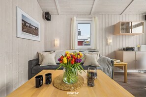 Ein gemütliches Wohnzimmer mit einem Holztisch, einer Couch mit Kissen, einem Strauß Tulpen und einem gerahmten Bild an der Wand.