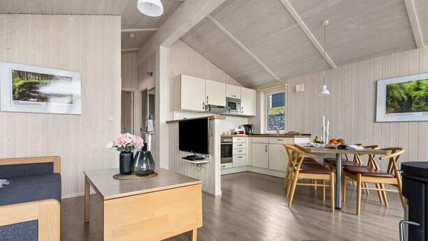 Una cocina amplia con armarios blancos, un comedor con sillas de madera y un televisor sobre una mesa de madera.