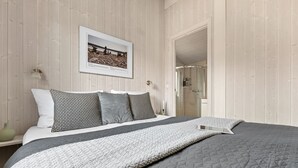 Un dormitorio ordenado con cama, almohadas, un cuadro enmarco y una puerta que da a un baño.