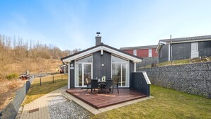 Una casa moderna con terraza, chimenea y un muro de piedra.