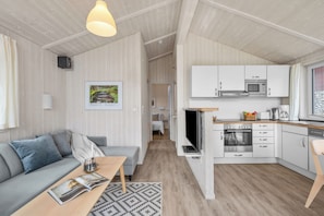 A modern interior with a sofa, coffee table, and a kitchen area featuring a microwave, oven, and cabinets.