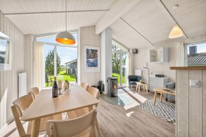 A modern interior with a dining area, a fireplace, and large windows offering a view of a garden.