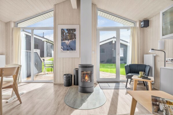 A modern interior with a central wood-burning stove, a dining area, and a large sliding glass door leading to an outdoor space.