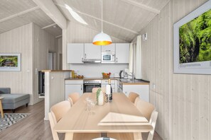 Une cuisine moderne avec des meubles blancs, un four à micro-ondes et un four traditionnel. On y trouve une table à manger avec des chaises et un luminaire suspendu.