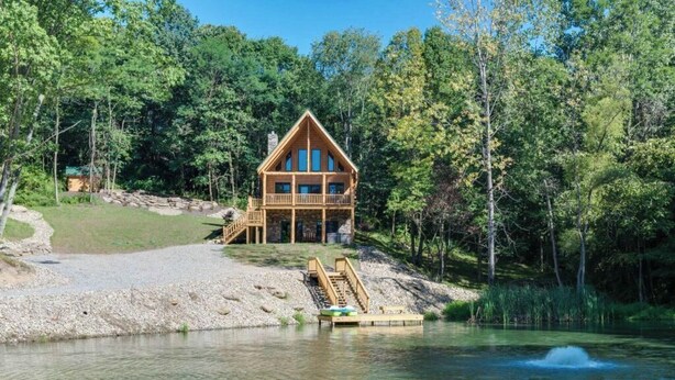 Una cabaña de madera con balcón, ubicada junto a un lago rodeado de árboles.