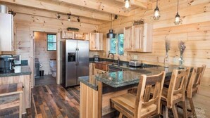 Interior de una cabaña de madera con zona de cocina que incluye un refrigerador, estufa y asientos en la barra.