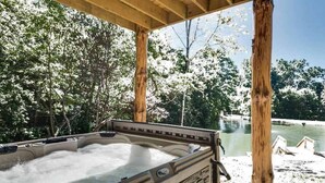 Un jacuzzi bajo una pérgola de madera con vistas a un lago y árboles nevados.