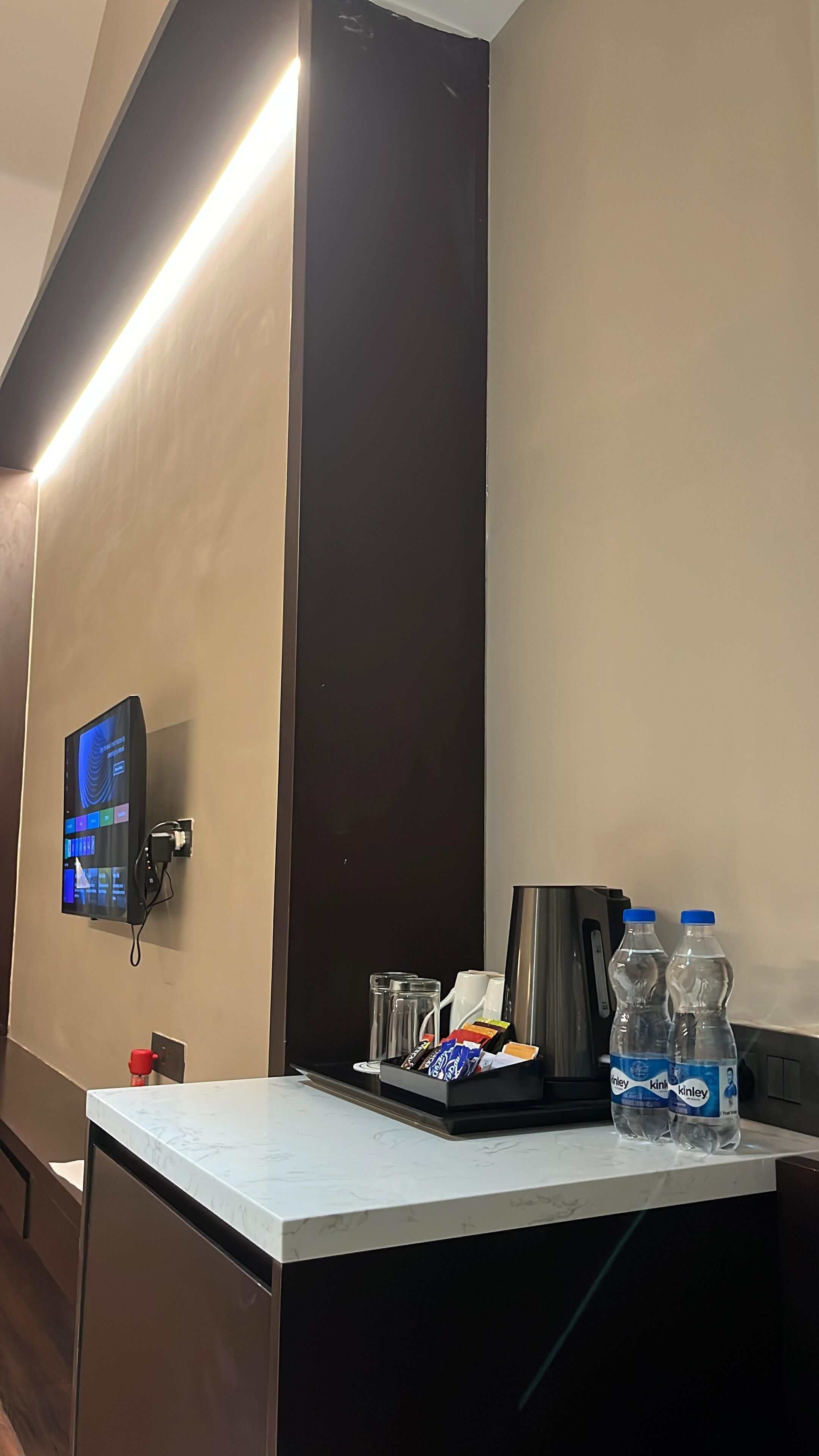 Een hotelkamer met een flatscreen televisie aan de muur, een minibar met water en snacks, en een koffiezetapparaat.