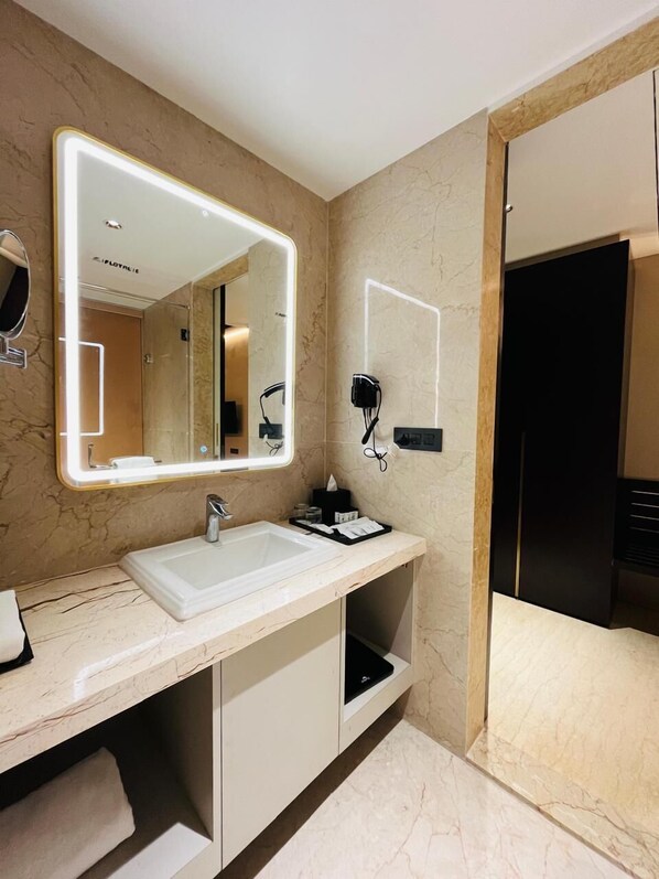 A modern bathroom with a large mirror, a sink, and a hairdryer on the wall. - Unique Resort & Lifestyle (Valsad)