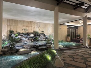 A serene indoor garden with a water feature, stone steps, and seating areas. - Unique Resort & Lifestyle (Valsad)