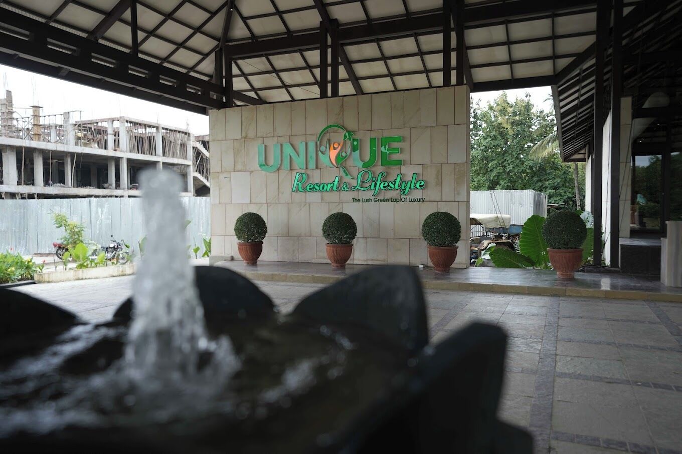 A building entrance with a sign reading "UNIQUE Resort & Lifestyle" and a water feature in the foreground.