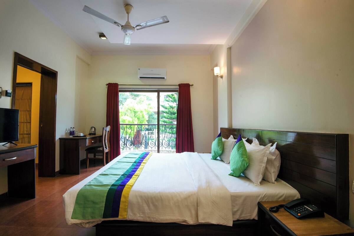 A hotel room with a bed, desk, chair, TV, and a balcony with a view.