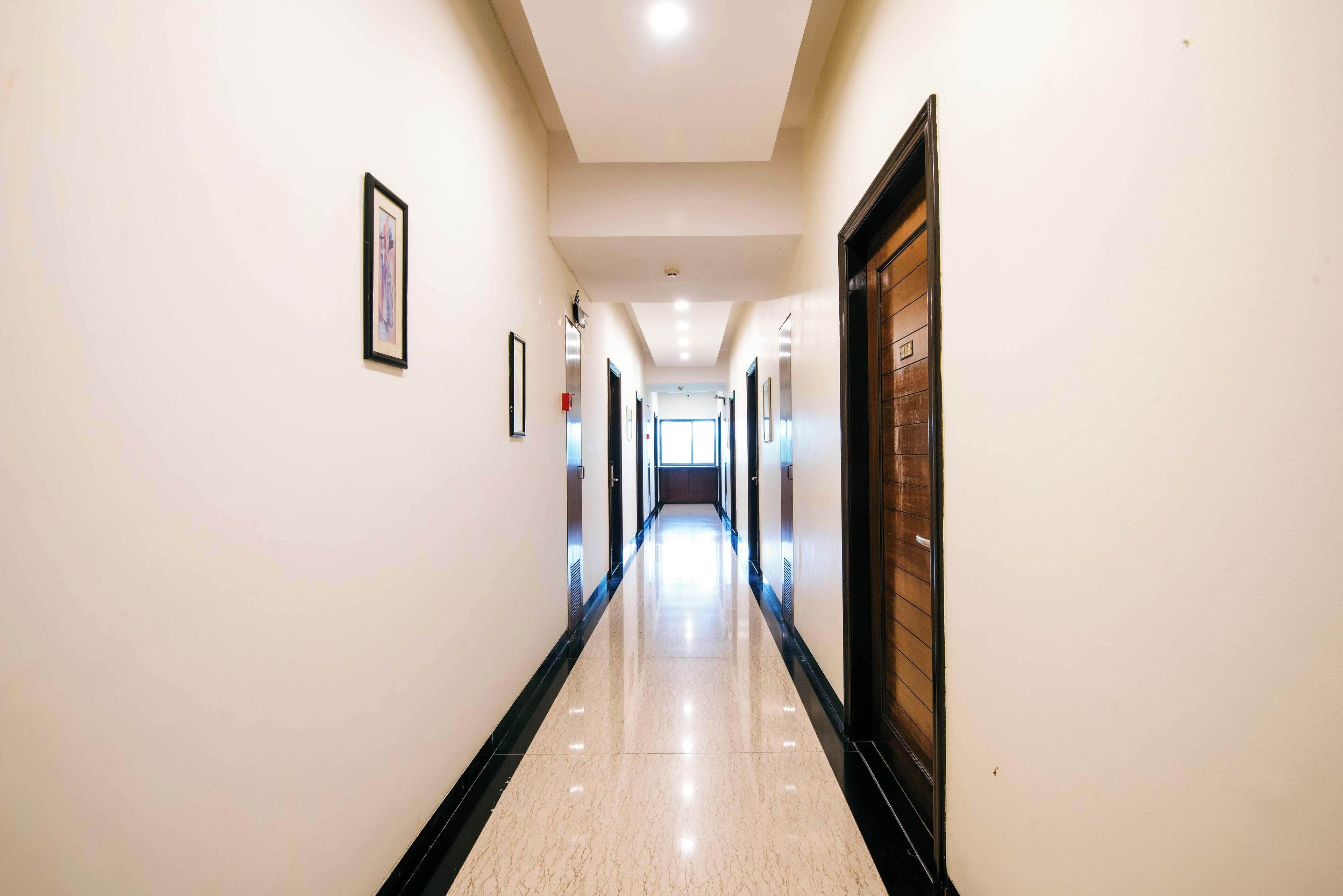 A long, narrow hallway with white walls and a shiny floor, leading to a door at the end.