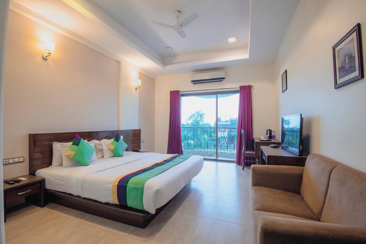 A hotel room with a bed, a TV, a sofa, and a balcony with a view.