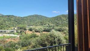 Un balcon donnant sur une colline parsemée d’arbres, avec un bâtiment visible au loin.
