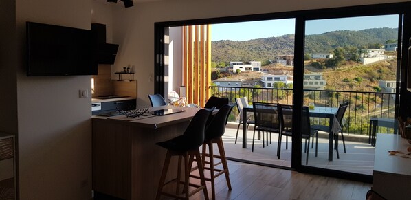 Una cocina moderna con una isla grande, un comedor con vistas a una colina y un balcón con mobiliario exterior.