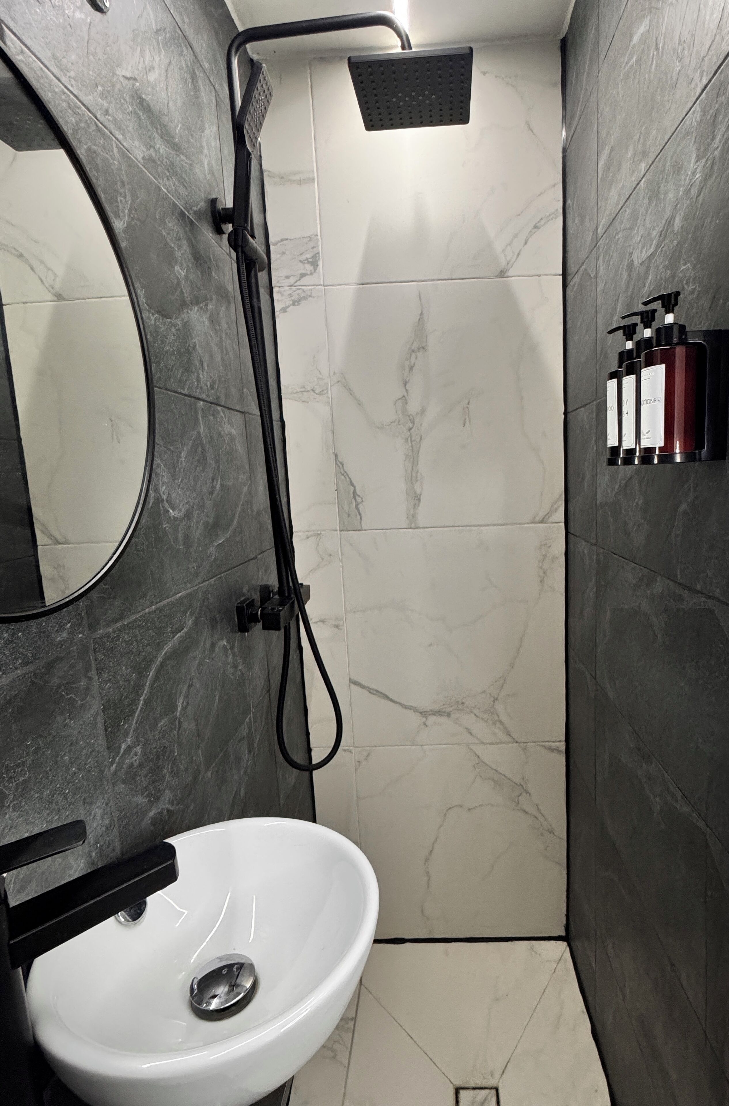 A bathroom with a white sink, a mirror, a shower with a black hose, and marble tiles.