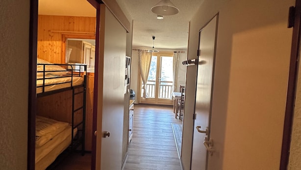 A narrow hallway with wooden flooring leading to a room with bunk beds.