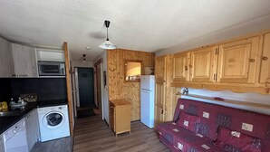 A compact kitchen with wooden cabinets, a washing machine, a microwave, and a refrigerator.