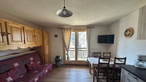 A cozy room with a wooden sofa, a dining table with chairs, a TV, and a window with curtains.