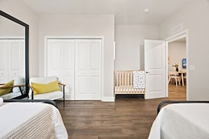 A bedroom with two beds, a crib, a chair, and a desk with a chair. - Ocala Downtown Square Apartment (Ocala)