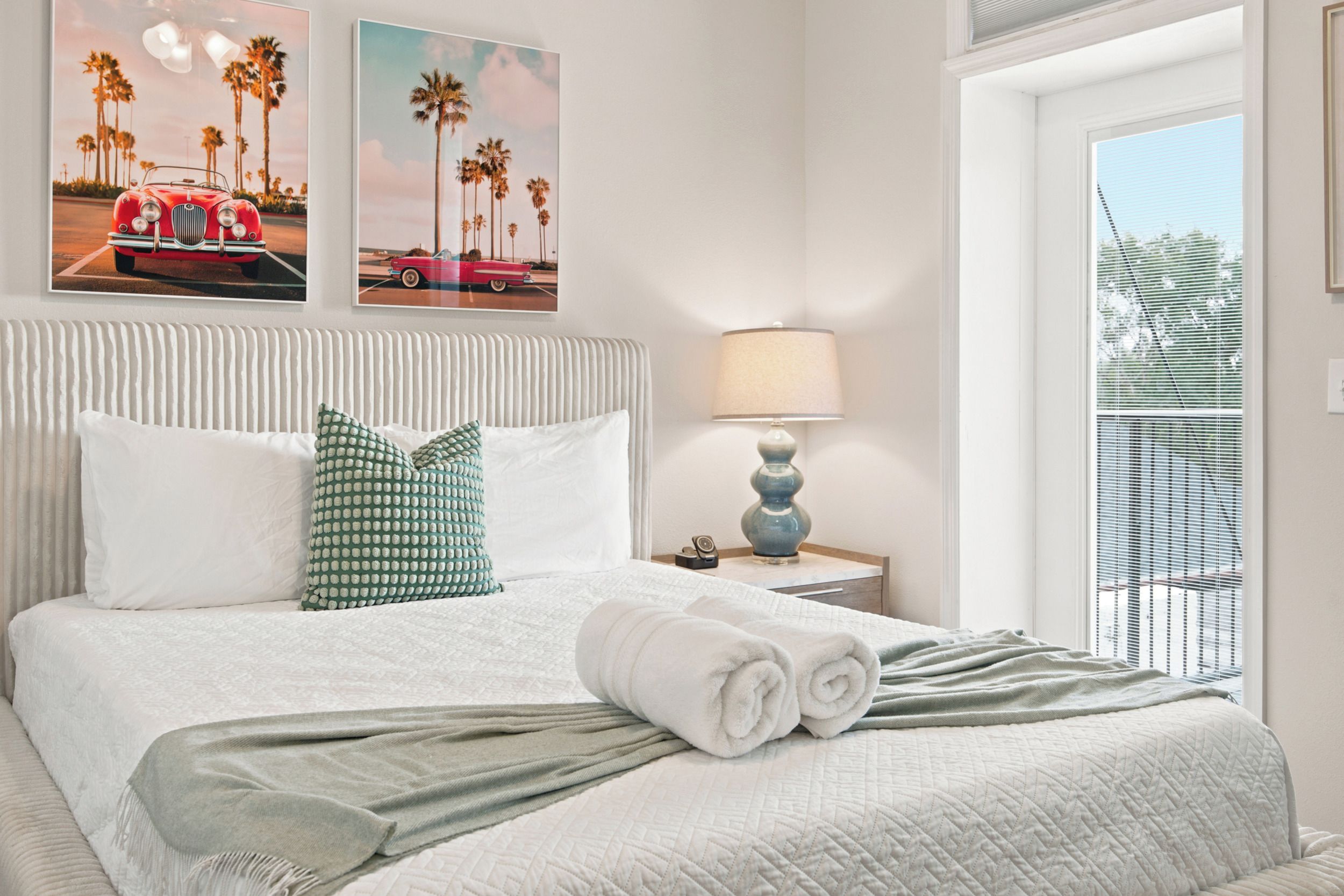 A hotel room with a bed, pillows, a lamp, and artwork on the wall.