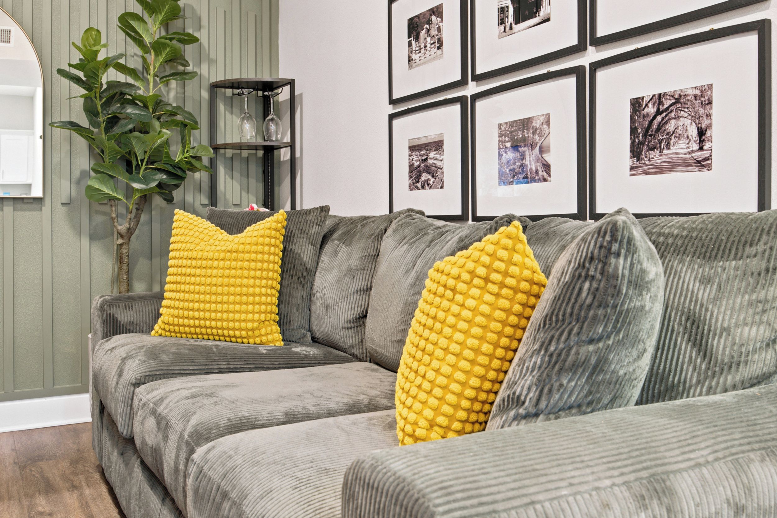A grey sofa with yellow textured cushions, a potted plant, and framed pictures on the wall.