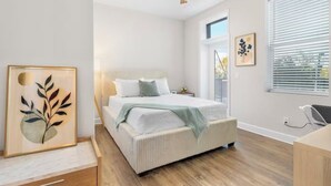 Un dormitorio con cama, ventilador de techo, ventana con persianas y un cuadro en la pared.