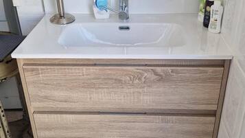A bathroom with a white sink, wooden cabinetry, and toiletries on the countertop.