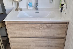 A bathroom with a white sink, wooden cabinetry, and toiletries on the countertop.