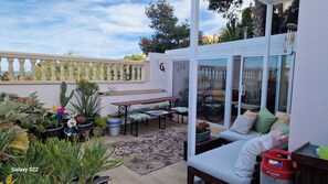 A patio area with a dining table, benches, and a sofa. There are potted plants and a decorative pinwheel. - The Fey Economy Apartment Gran Alacant (Santa Pola)