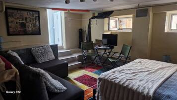 A compact room with a sofa, a bed, a small table, and a TV.