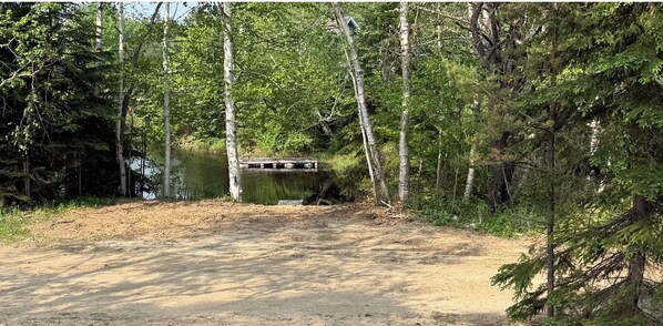 A dirt path leading to a bridge over a body of water, surrounded by dense forest.