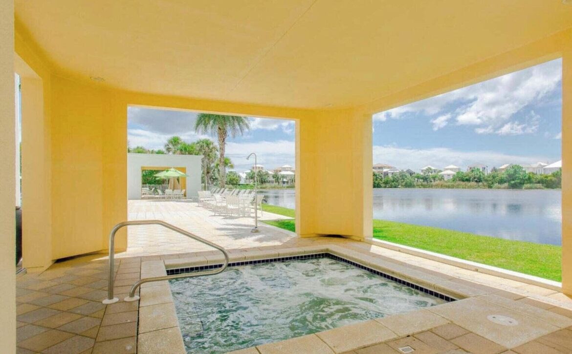 Un área de spa con hidromasaje, piscina y vistas a un lago y palmeras.